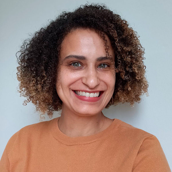 Foto de Larissa Aliberti sorrindo, uma mulher de olhos claros e cabelos cacheados