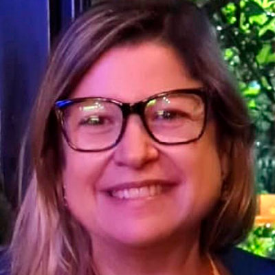 Foto de Marta Durante, uma mulher de pele clara e cabelos claros, lisos e compridos. Ela usa óculos de grau com moldura escura