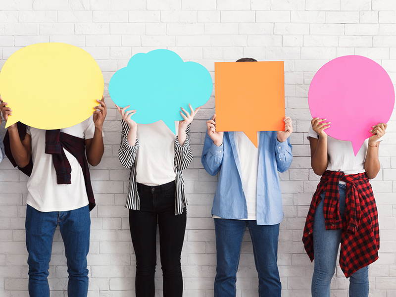 Foto com adolescentes diversos em pé, lado a lado, segurando balões de fala coloridos