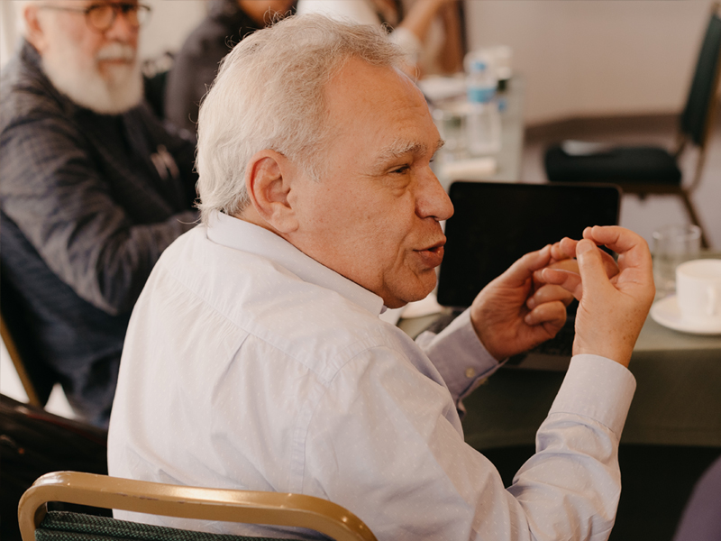 Foto de Lino de Macedo, um homem de pele clara e cabelos brancos de perfil, gesticulando.