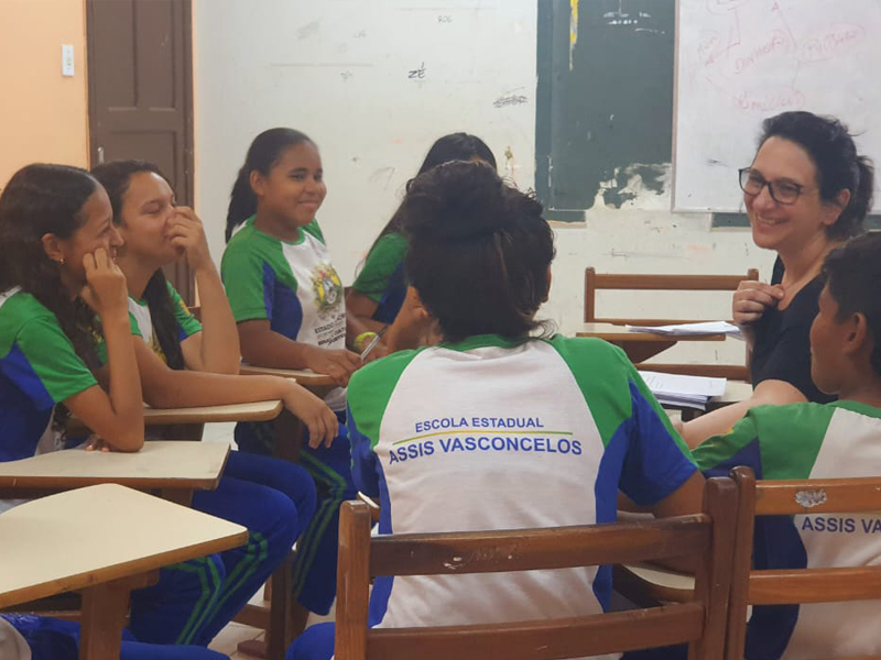Foto de crianças diversas e uma mulher em volta de uma mesa.
