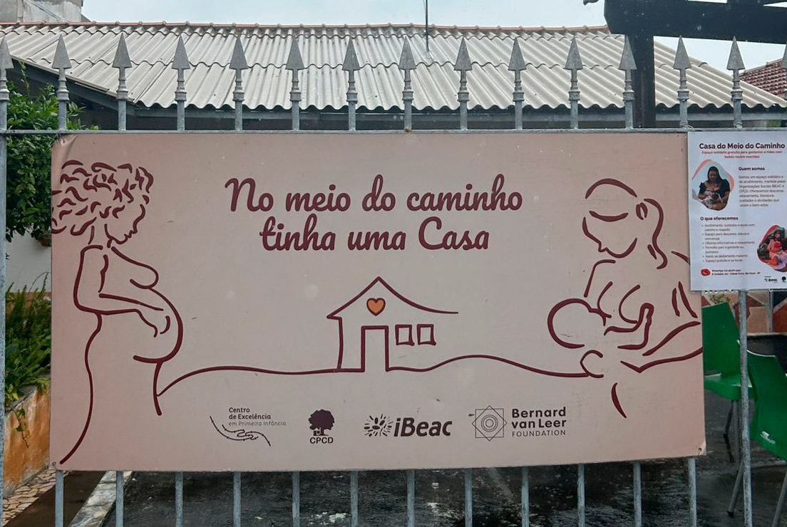 Grade com um banner colado sobre ela. Há o texto: "No meio do caminho tinha uma casa), com diversos logos incluindo o do Ibeac.